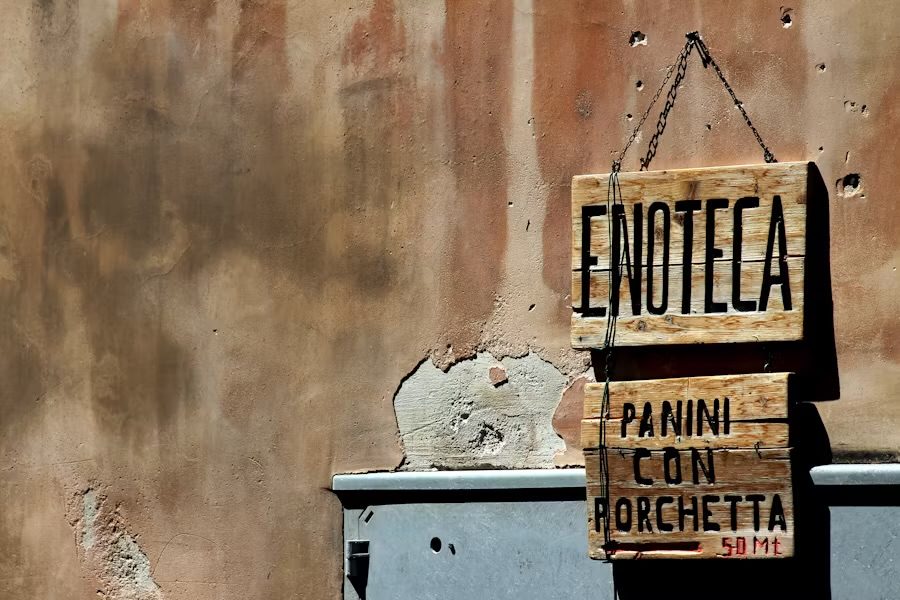 Handgeschriebenes Holzschild «Enoteca — Panini con Porchetta» an einer verputzten Wand