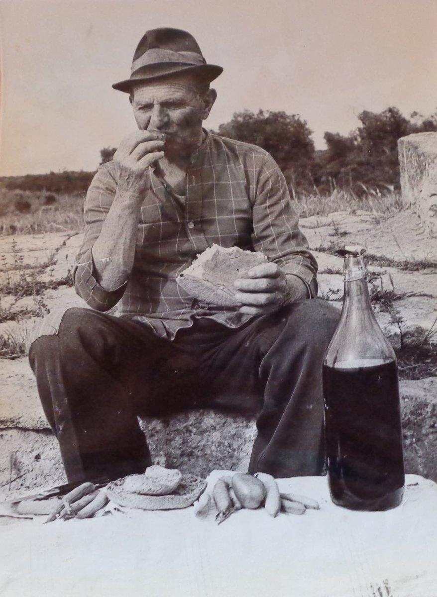 Sonjas Grossvater in Apulien, mit Hut auf einem Stein sitzend, Brot in den Händen